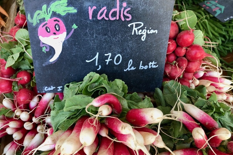 Bunches of radishes at a market in France, with a cute cartoon radish sign.