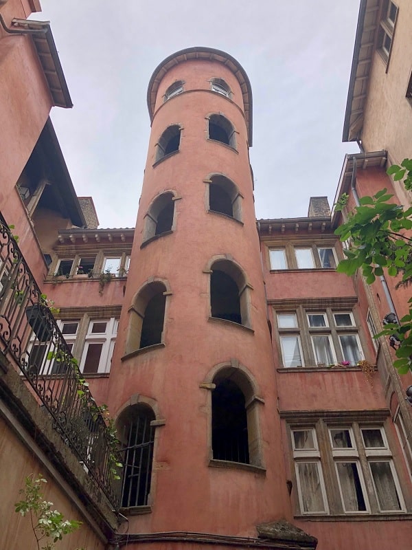 One of the beautiful traboules in Lyon France, The walls are reddish in color, and a tall tower with multiple windows is in the center.