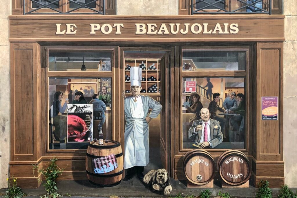 Close up of a Lyon mural depicting a restaurant scene with chef Paul Bocuse in the doorway. The restaurant name is Le Pot Beaujolais and there are wine barrels in front of the restaurant.