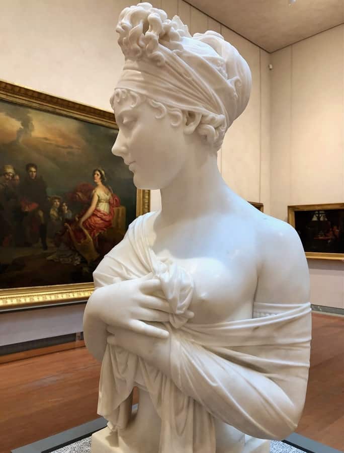 Close-up of a classical statue of a young woman with her hair tied up, holding a sheet to cover herself.  Statue is located in the Musee des Beaux Arts in Lyon France.