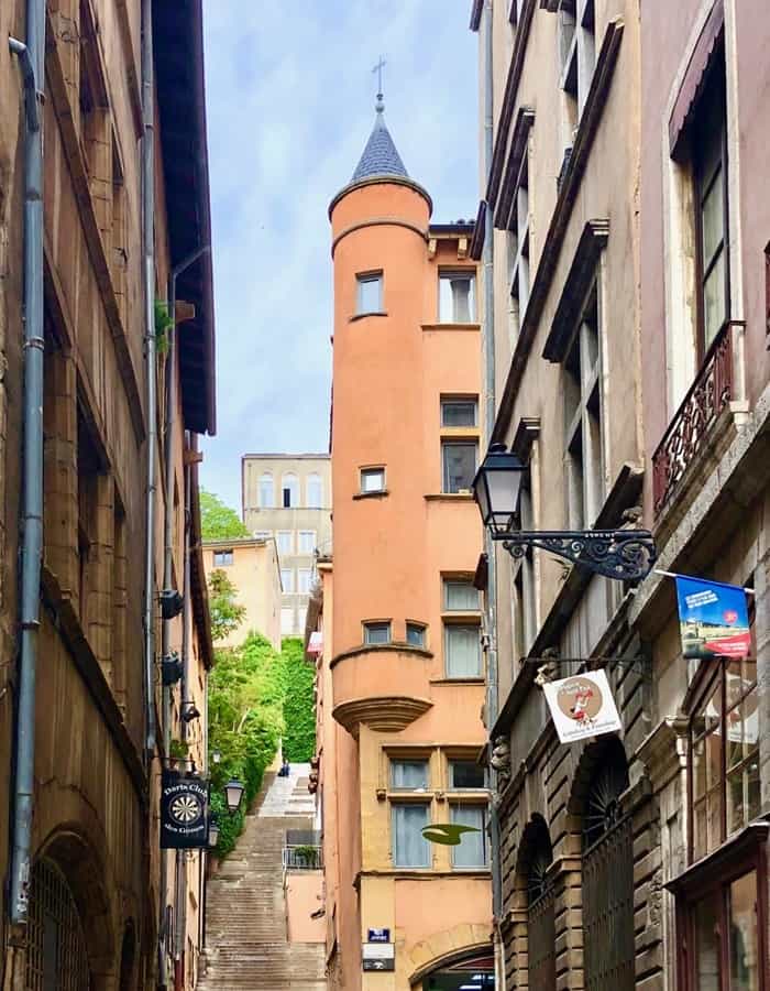 Alleyway in Vieux Lyon opens out onto a stairway climbing Fourviere Hill and a red tower with a peaked top.