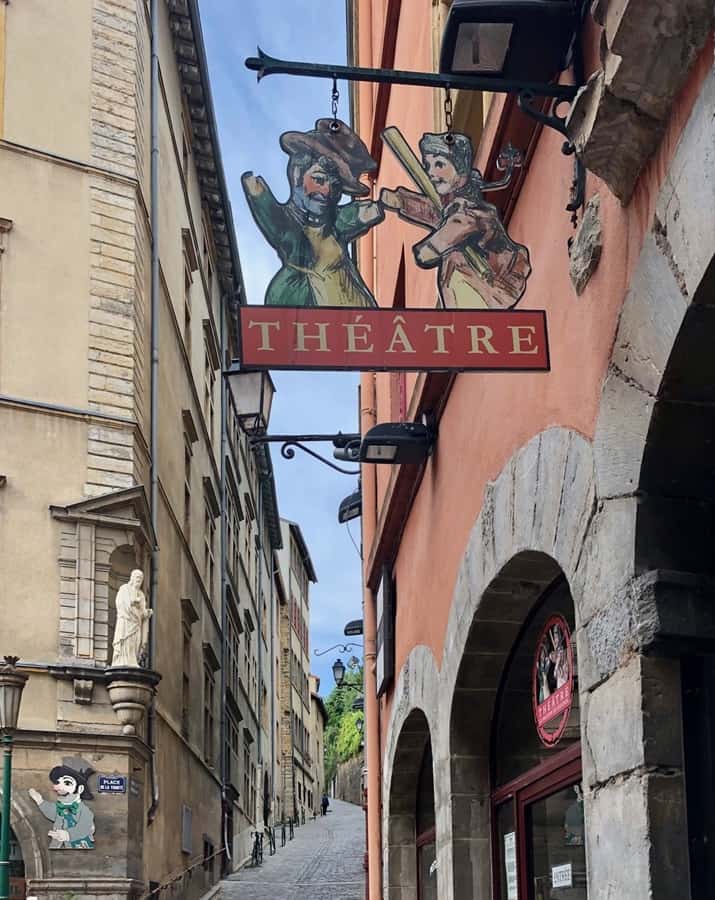 The picture-perfect streets of Vieux Lyon, with red buildings.  A sign for a puppet theater hangs from overhead.