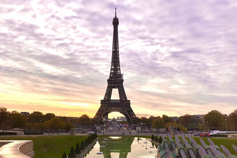 Eiffel Tower in Paris at sunrise, set against clouds tinted pink and purple.